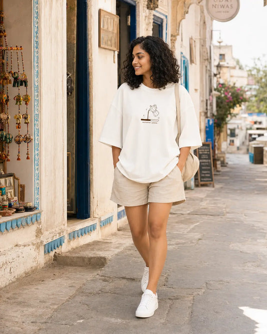 Woman walking on a street wearing a white t-shirt and beige shorts.