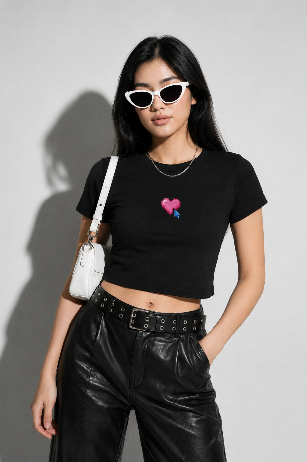 Woman wearing a black t-shirt with a colorful heart design, black pants, and sunglasses against a gray background.