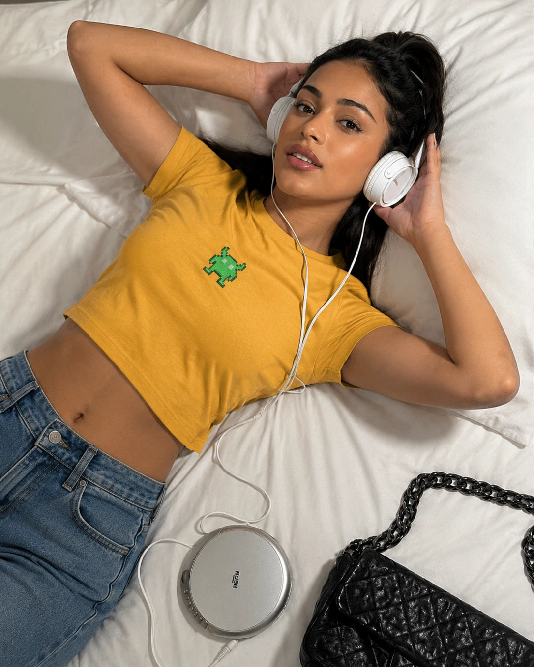 Woman lying on a bed wearing headphones and a yellow shirt with a green logo.