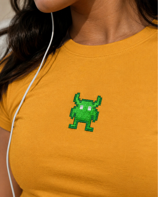 Person wearing a mustard yellow t-shirt with a green pixelated character on the chest.