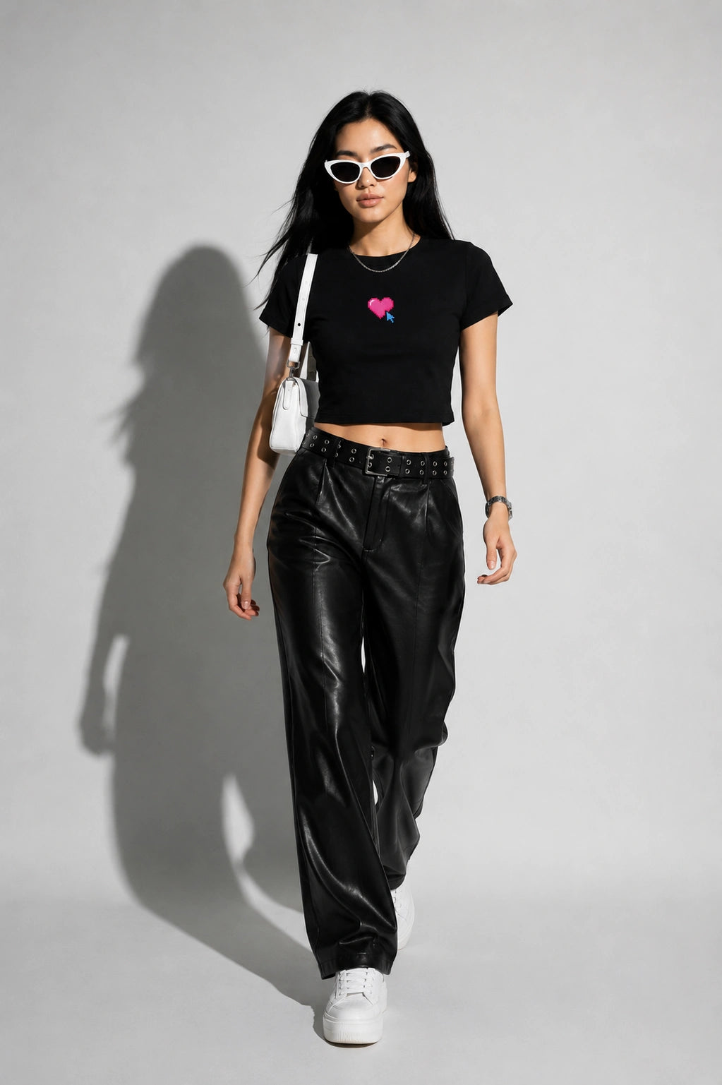 Woman wearing a black t-shirt with a pink heart design, black leather pants, and white sneakers on a gray background.