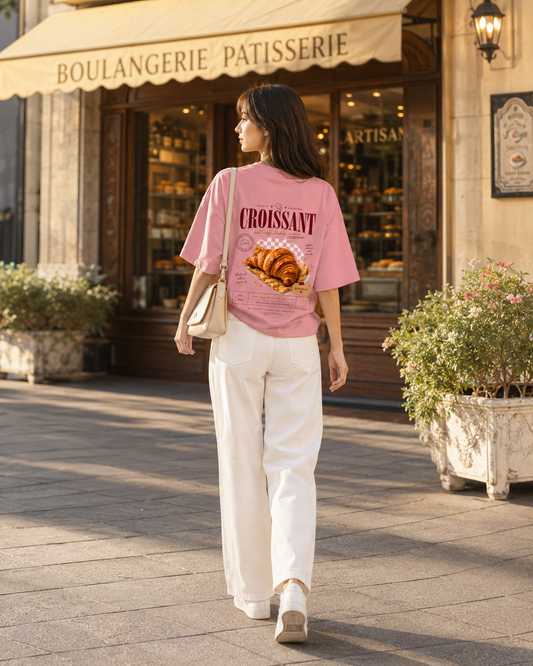 Woman walking past a bakery wearing a pink t-shirt with a croissant graphic.
