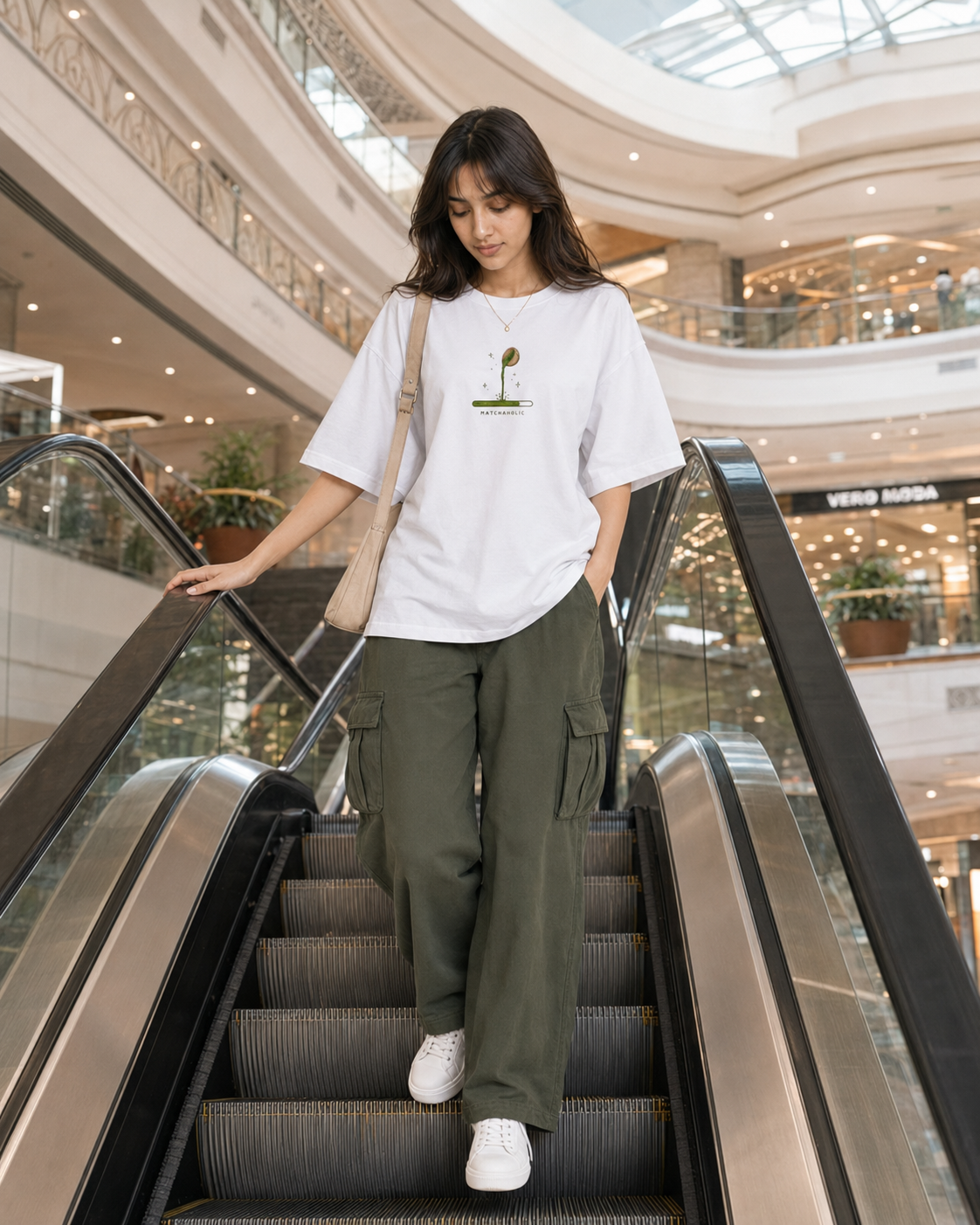Woman in a white t-shirt and green cargo pants standing on an escalator in a mall.