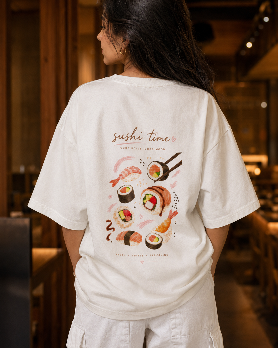 Person wearing a white t-shirt with sushi design and text in a restaurant setting