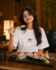 Woman in a sushi-themed t-shirt enjoying sushi at a restaurant.